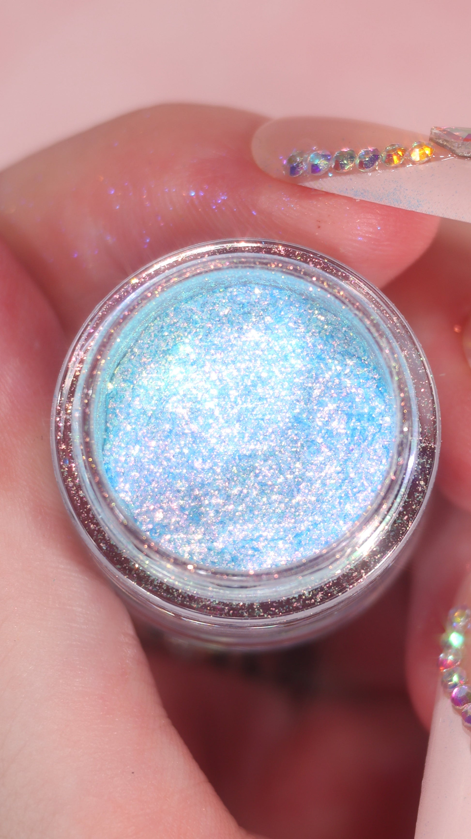 Jar of blue glitter held in a hand with pink background