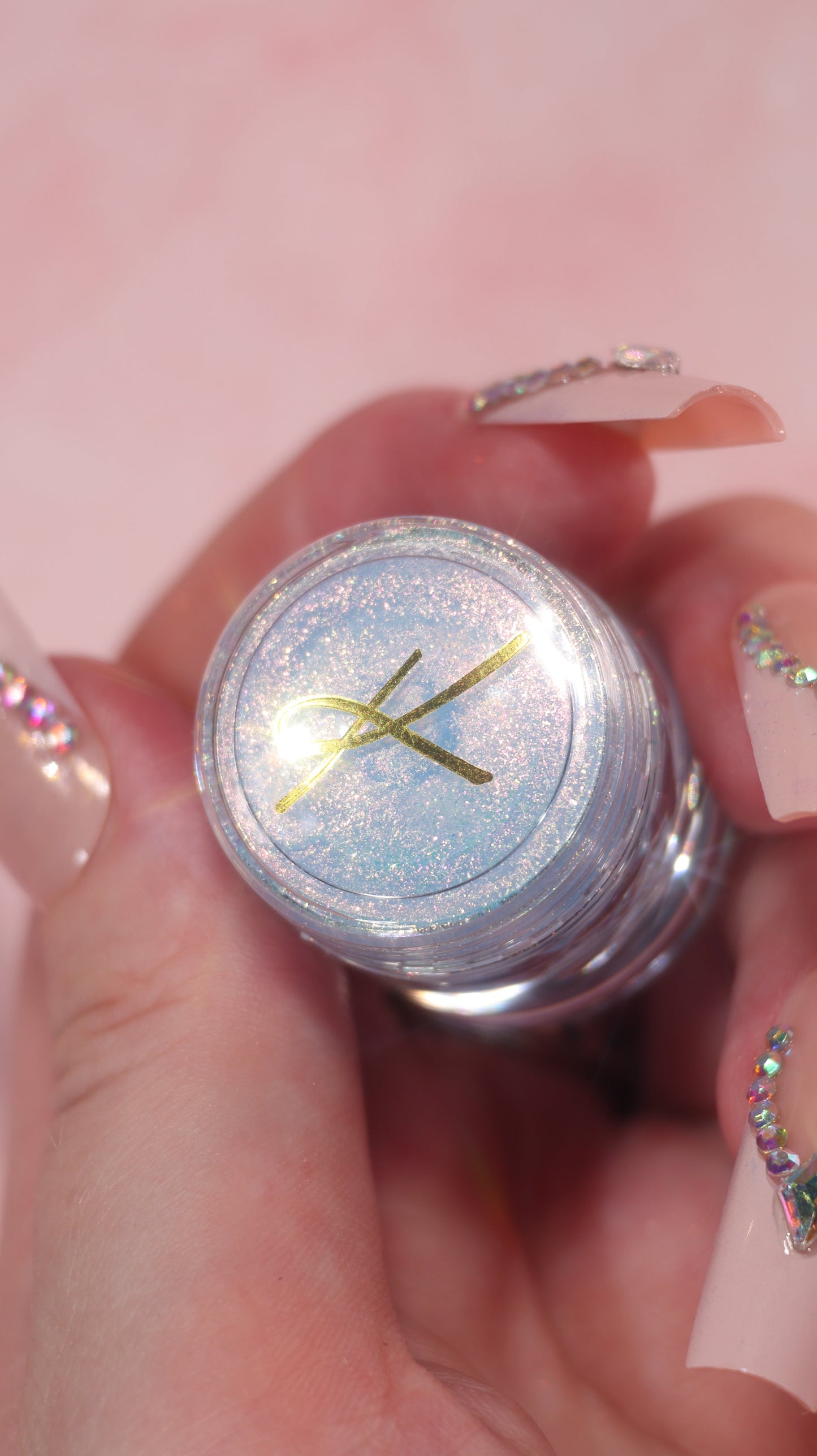 Silvery jar of sparkly powder held in hand with pink background
