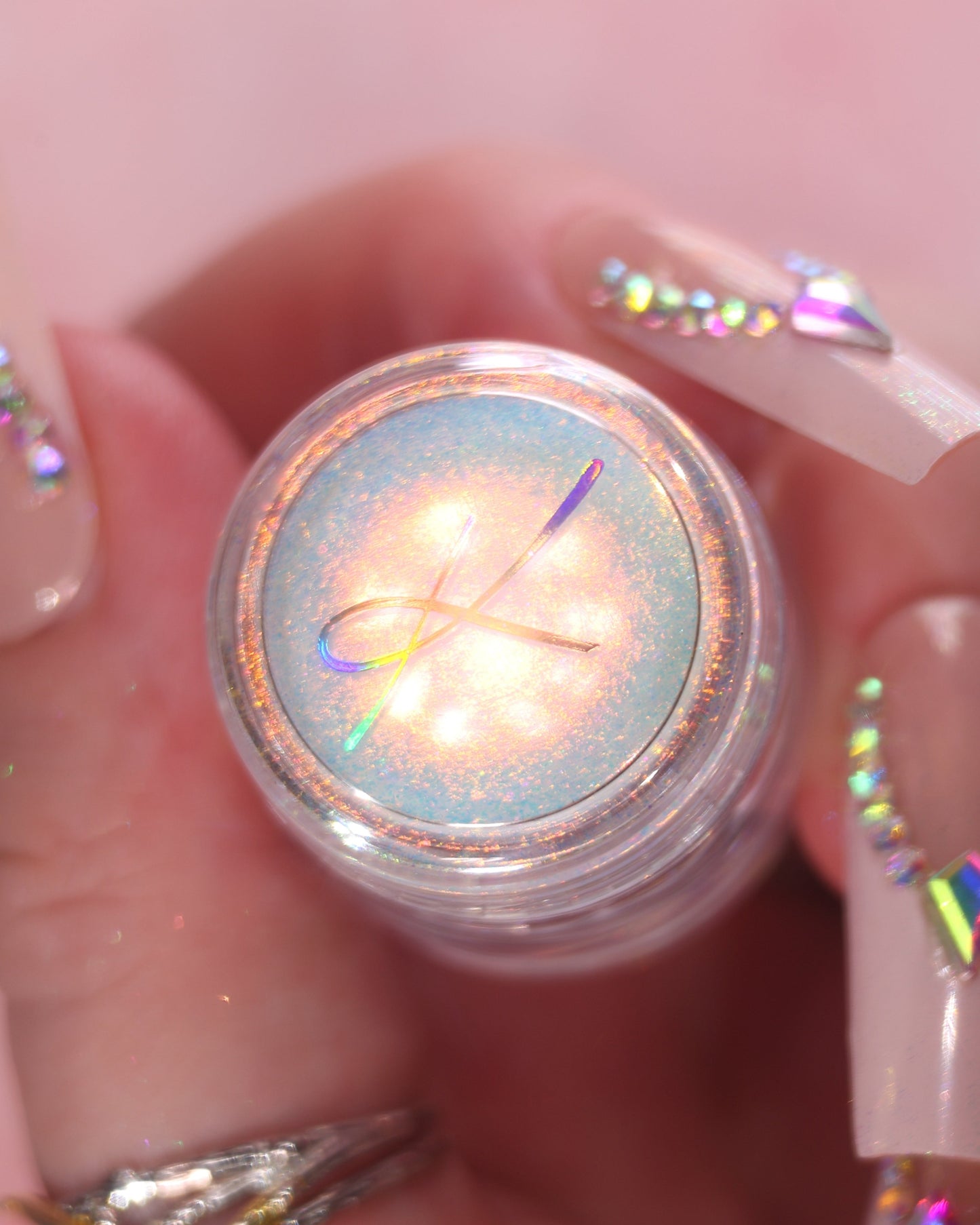 Close-up of a hand with glittery nail polish holding a jar of loose sparkly eyeshadow