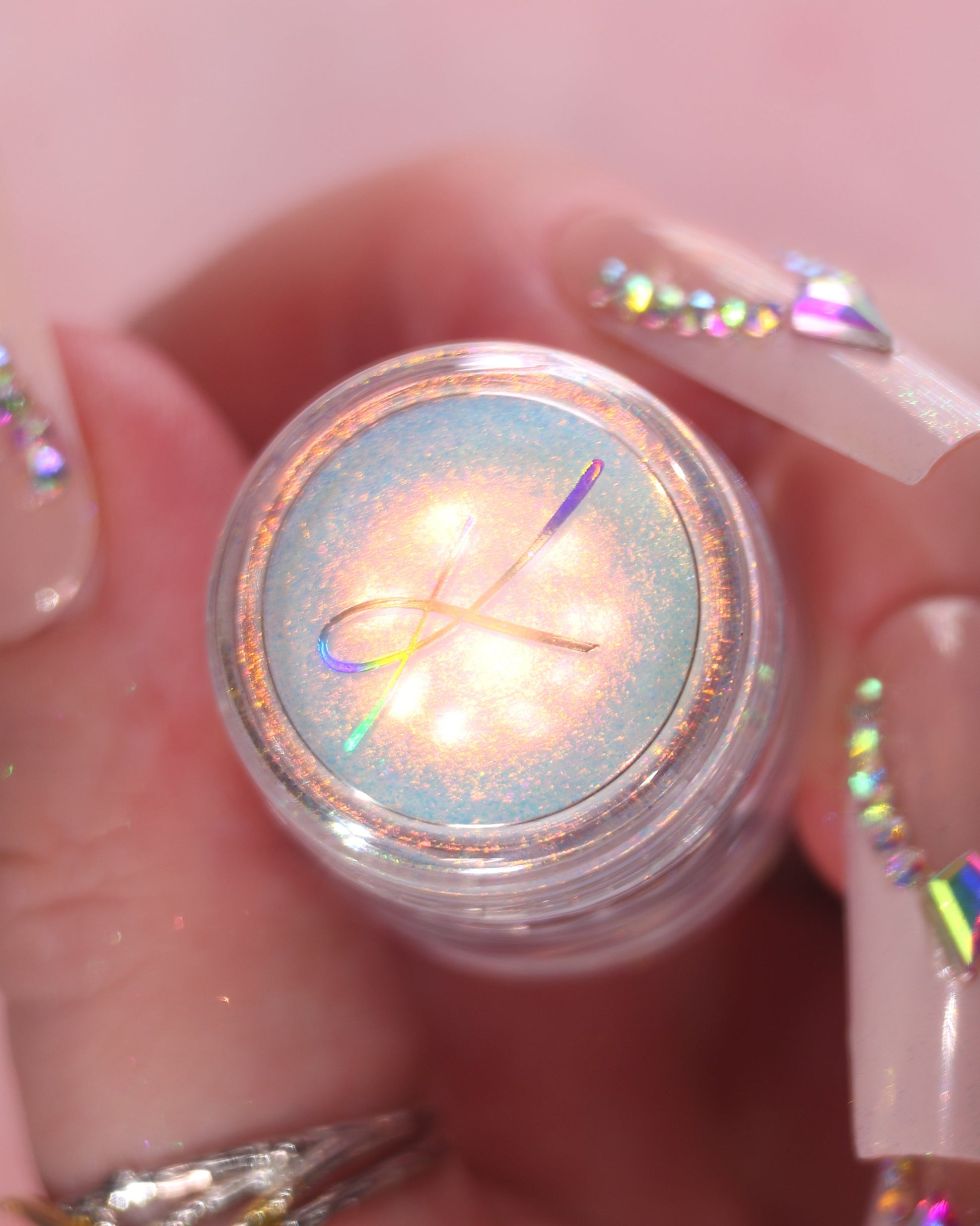 Close-up of a hand with glittery nail polish holding a jar of loose sparkly eyeshadow