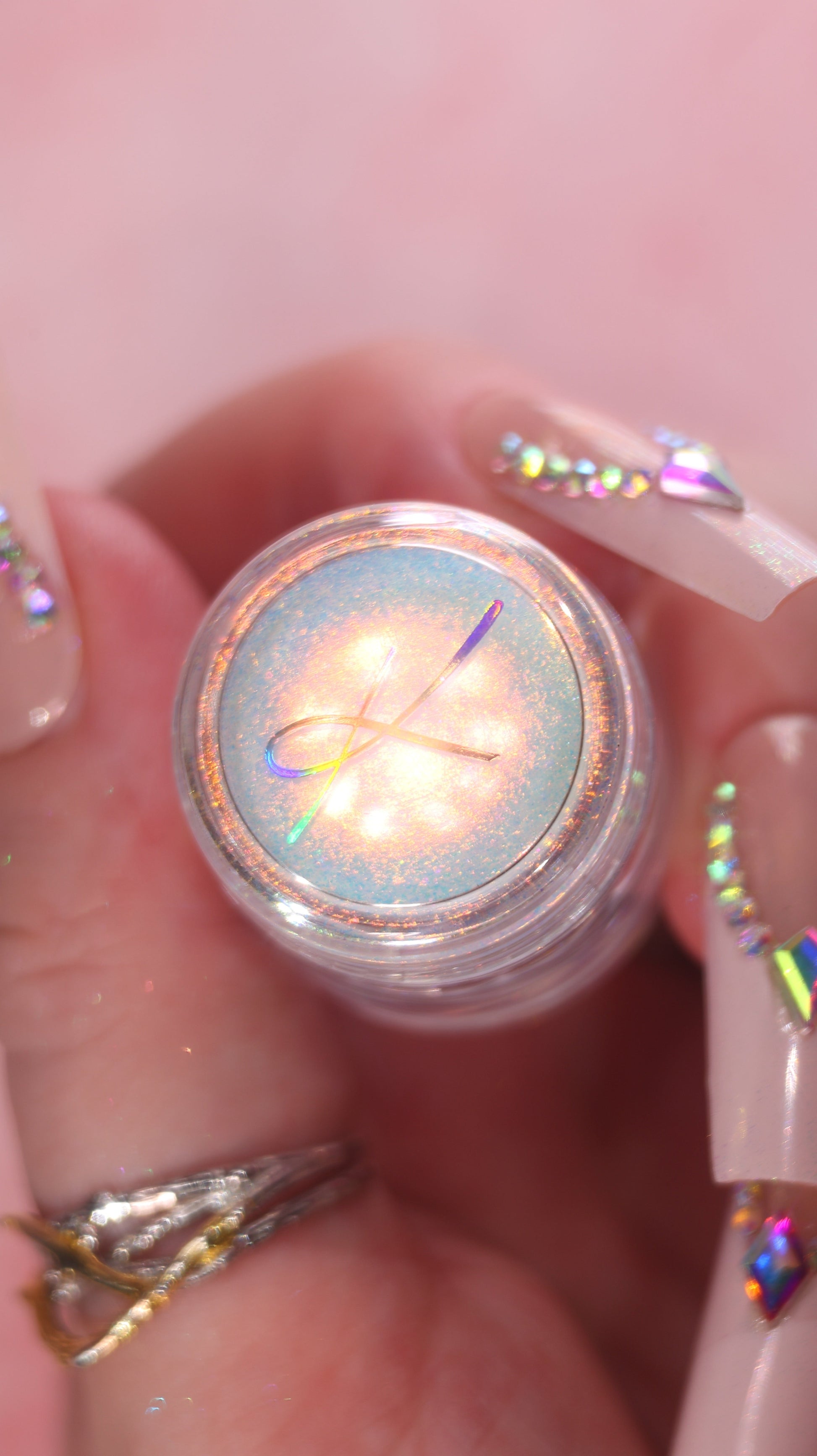 Close-up of a small pot of loose pigment with a colorful, iridescent surface held between fingers.