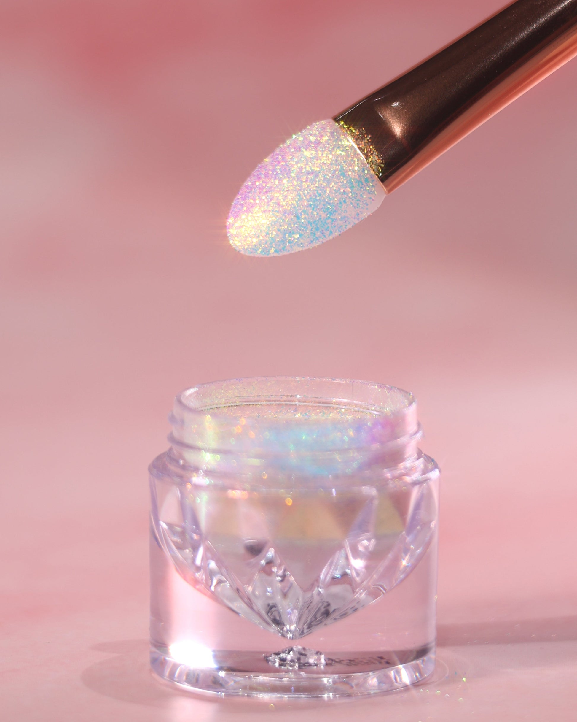 Makeup brush with glittery powder over a jar of the same powder on a pink background