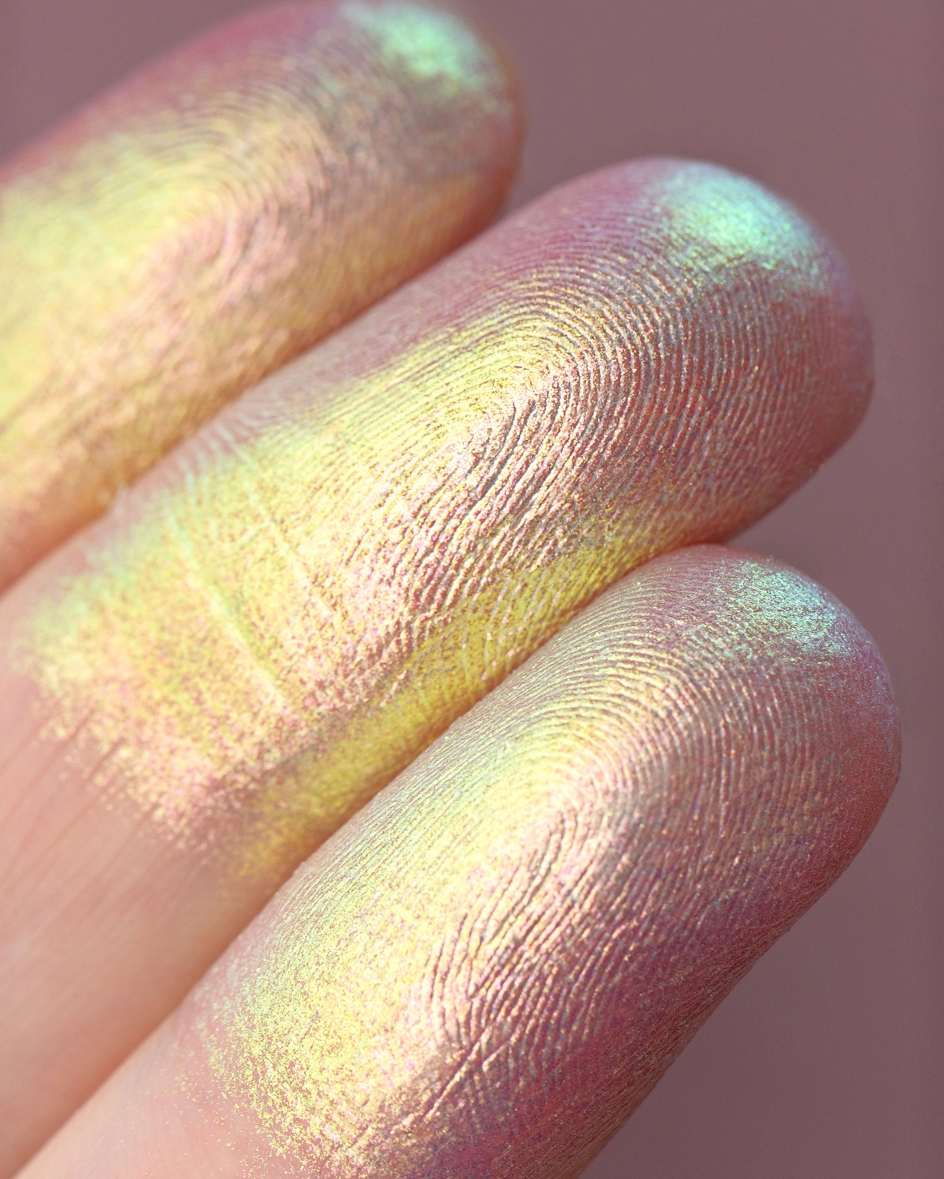 Close-up of a hand with colorful makeup on the fingers against a pink background