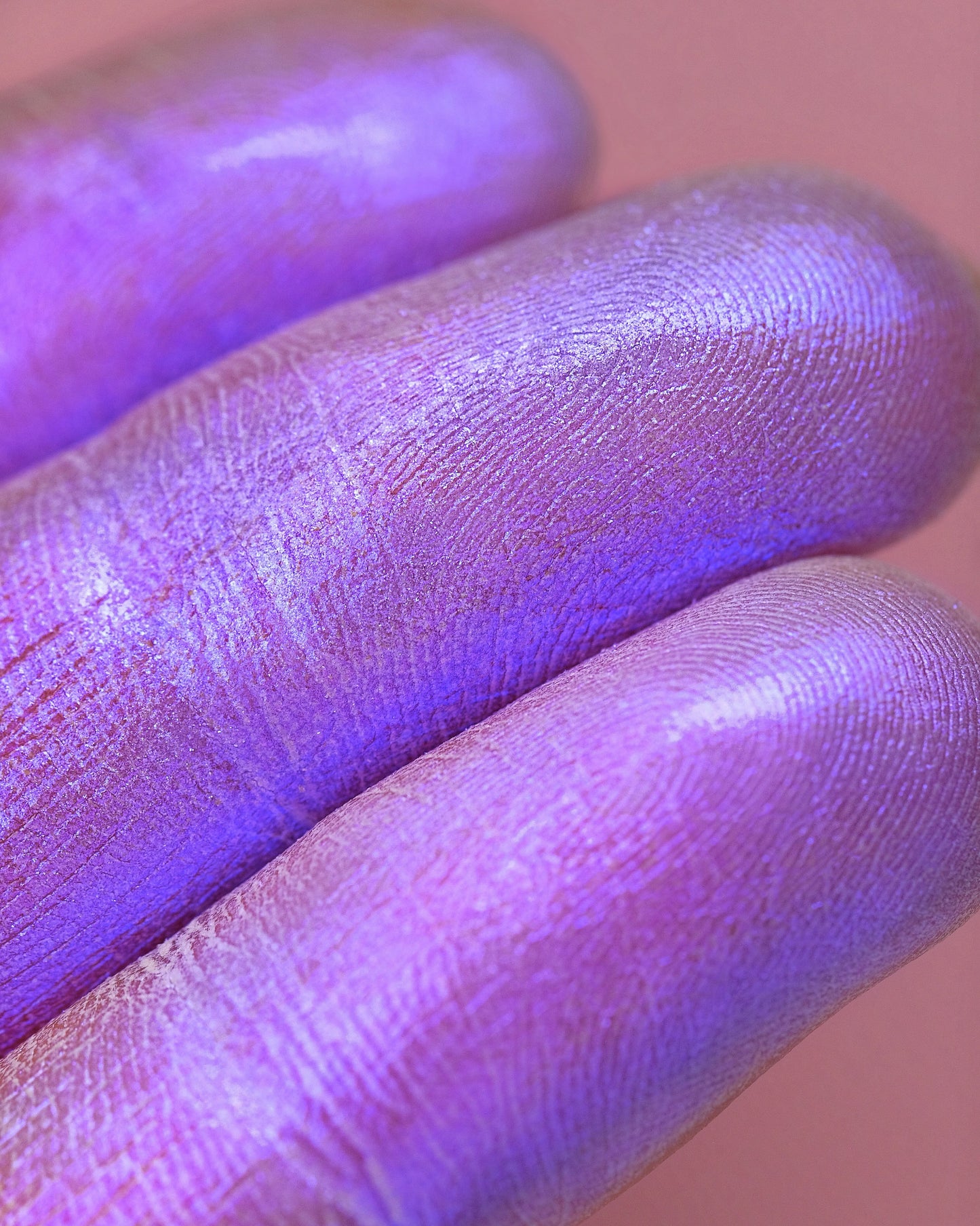 Close-up of a hand with purple sparkly eyeshadow on a pink background