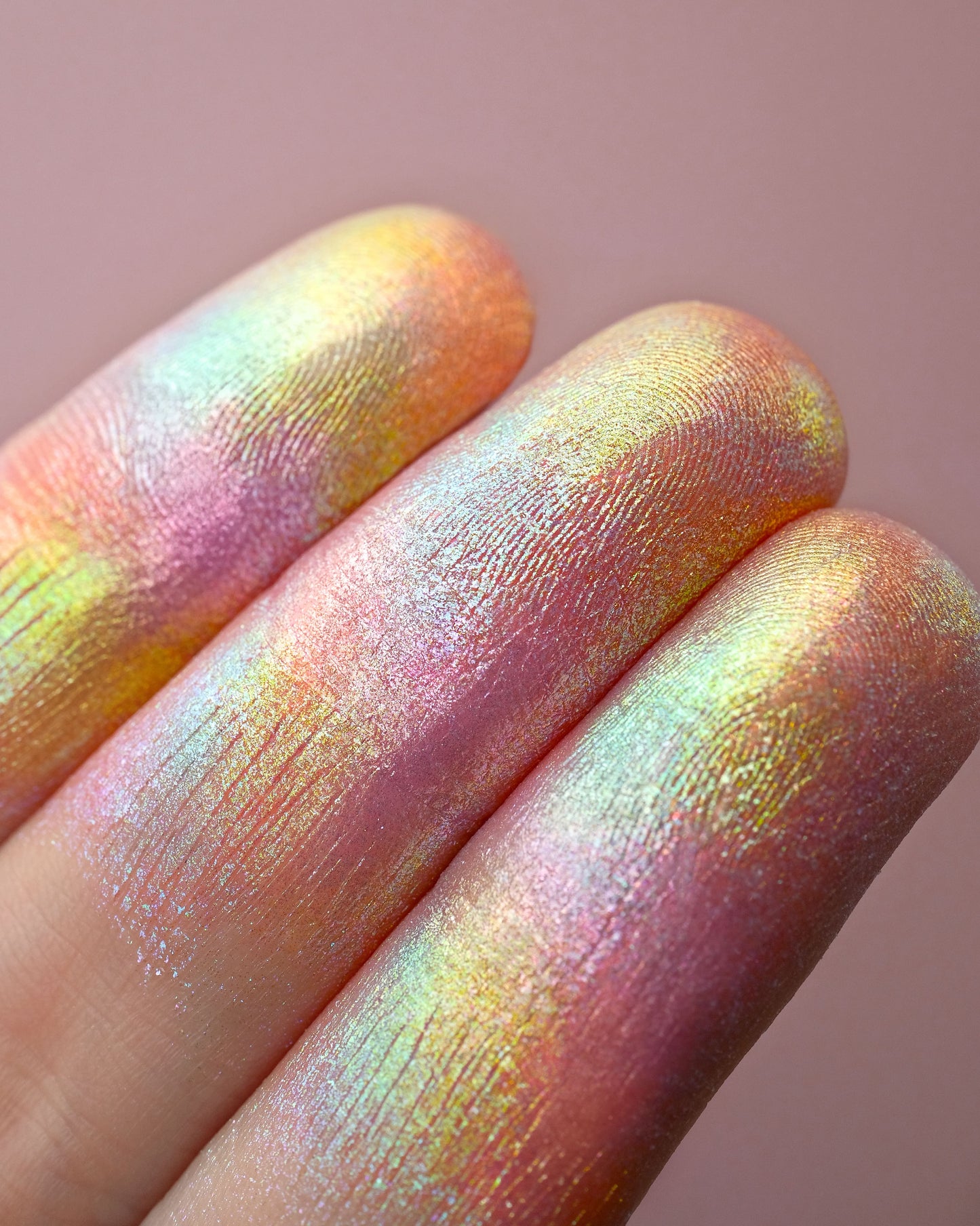 Close-up of a hand with colorful, iridescent makeup on a pink background